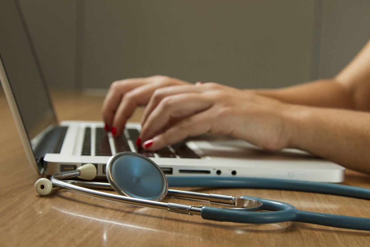 Profesional de la salud trabajando en un portátil junto a un estetoscopio